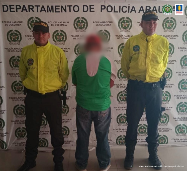 n la fotografía se aprecia el capturado de espaldas junto a dos uniformados de la Policía Nacional. En la parte posterior se observa el banner que identifica al Departamento de Policia Arauca