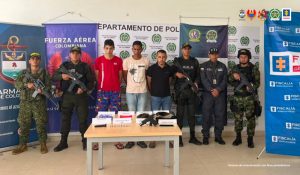 En la imagen se aprecia a los tres capturados junto a un investigador del CTI y uniformados de la Policía, Armada y Ejército Nacional. En la parte posterior se observan los banners que identifican a la Fiscalía General de la Nación, Fuerza Aérea, Ejército, Armada y Policia Nacional.