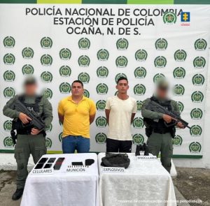 Se observa a los dos capturados junto a dos uniformados del Gaula de la Policía Nacional. Frente a ellos dos mesas donde se ubica el material incautado. Detrás del banner que identifica a la estación de Policía de Ocaña