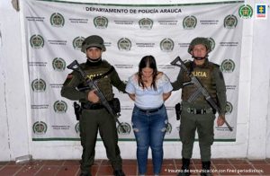 Se observa a la capturada junto a dos uniformados de la Policía Nacional. Detrás de ellos el banner que identifica a la Policía Nacional.