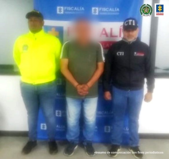 En la imagen aparece el capturado junto a un investigador del CTI y de la SIJIN. En la parte posterior se observa el banner que identifica a la Fiscalía General de la Nación