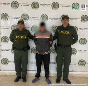 En la imagen se observa al capturado junto a dos uniformados de la Policía Nacional. En la parte posterior el banner que identifica a la Policía Nacional.