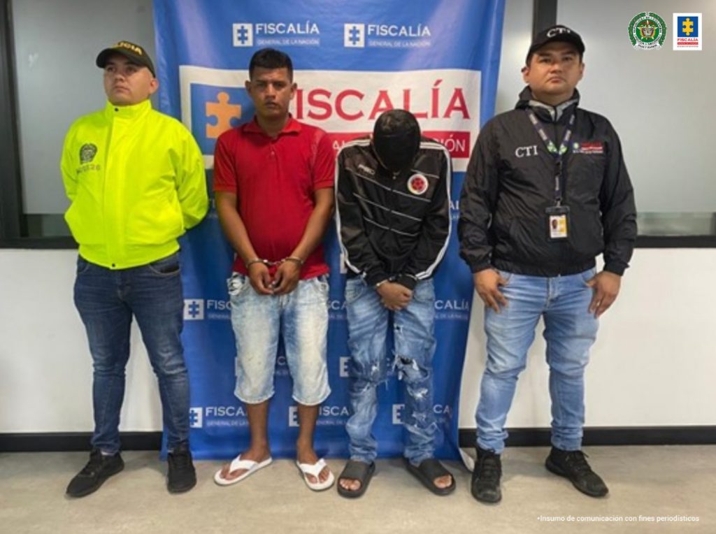 En la imagen se aprecia a los dos capturados junto a un investigadore del CTI y de la Sijin. En la parte posterior se observa el banner que identifica a la Policía Nacional.