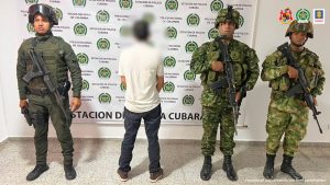  En la imagen se observa al capturado de espaldas junto a uniformados de la Policía y Ejército Nacional. En la parte posterior se observa el banner que identifica a la Estación de Policía de Cubará (Boyacá).