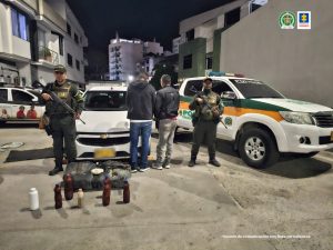 Se visualiza a los dos hombres de espaldas junto a uniformados de la Policía Nacional. Frente a ellos la sustancia incautada. Detrás de ellos una patrulla de la Policía Nacional 