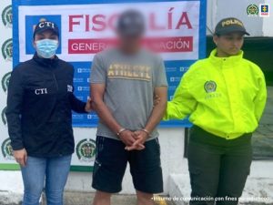 En la gráfica aparece el capturado junto a una investigadora del CTI y una uniformada de la Policía Nacional. Detrás de ellos el banner que identifica a la Fiscalía General de la Nación.