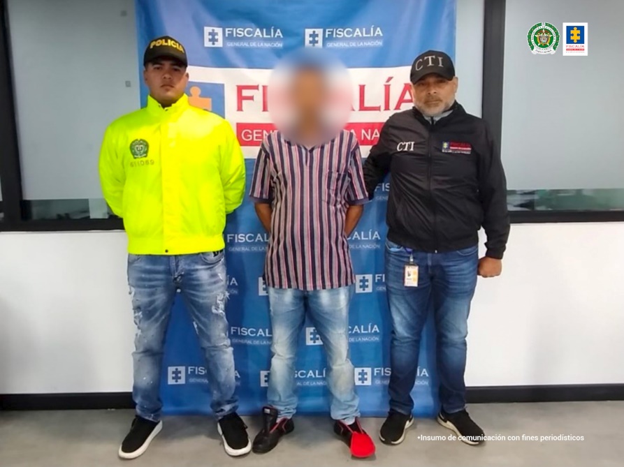 En la fotografía se aprecia al caputarado con el rostro difuminado junto a investigadores de la SIJIN y del CTI. Detrás de ellos el bannner que identifica a la Fiscalía General de la Nación
