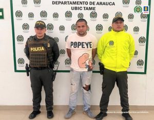 En la imagen se aprecia al capturado junto a dos uniformados de la Policía Nacional. Detrás de ellos un banner que identifica al Departamento de Policía en Tame (Arauca)
