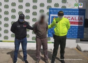 Se observa al capturado junto a un investigador del CTI y un uniformado de la Policía Nacional. Detrás se ubican los banners que identifican a la Policía Nacional y a la Fiscalía General de la Nación.