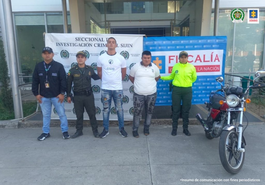 Se aprecia a los dos capturados junto a un investigador del CTI y dos uniformados de la Policía Nacional. En la parte posterior los banners que identifican a la Policía Nacional y a Fiscalía General de la Nación