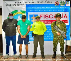 Se visualiza el capturado junto a un investigador del CTI y dos uniformados de la Policía y Ejército Nacional. Detrás de ellos los banners institucionales de la Policía Nacional y Fiscalía General de la Nación.