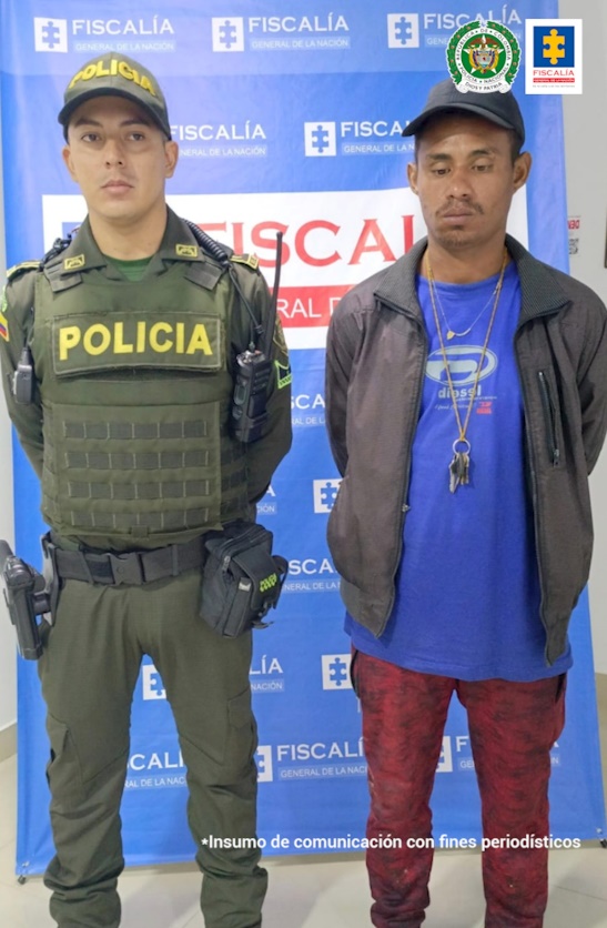 Se observa el capturado junto a un uniformado de la Policía Nacional. En la parte posterior se observa el banner que identifica a la Fiscalía General de la Nación.