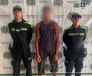 Se observa al capturado con el rostro difuminado junto a dos uniformados de la Policía Nacional. Detrás de ellos el banner que identifica a la Policía Nacional.
