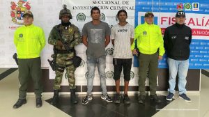 En la imagen se observa a los capturados junto a uniformados de la Policía, Ejército Nacional y a un investigador del CTI. Detrás de ellos se encuentran los banners que identifican a la Policía, Ejército Nacional y Fiscalía General de la Nación.