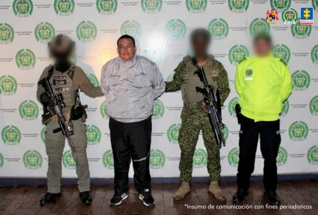 Se visualiza al capturado junto a uniformados de la Policía y Ejército Nacional. Detrás de ellos el banner que identifica a la Policía Nacional.