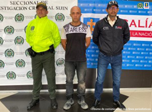 La imagen muestra al capturado junto a un investigador del CTI y un uniformado de la Policía Nacional. Detrás hay banners que identifican a la Policía Nacional y a la Fiscalía General de la Nación.