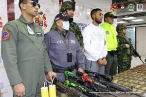 En la imagen se observa al capturado junto a un investigador del CTI y uniformados de la Fuerza Aérea, Ejército y Policía Nacional. Frente a ellos una mesa donde se aprecia los fusiles y la munición incautada.