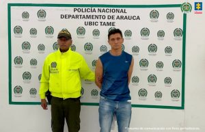 El capturado es visto junto a un uniformado de la policía nacional. Detrás del cartel que identifica a la Policía Nacional en Tame (Arauca)