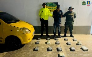 Se visualiza al capturado junto a dos uniformados de la Policía Nacional. Frente a ellos los paquetes de sustancias estupefacientes incautados y el vehículo en que se desplazaba.