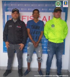 En la fotografía aparece el capturado junto a un investigador del CTI y de la SIJIN de la Policía Nacional. Detrás se observa el banner de la Fiscalía General de la Nación.