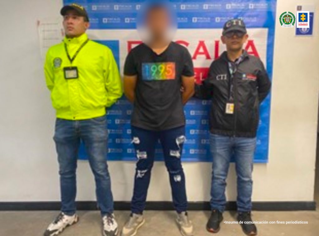 En la imagen se observa el procesado junto a un investigador del CTI y de la Sijin. En la parte posterior se aprecia el banner que identifica a la Fiscalía General de la Nación