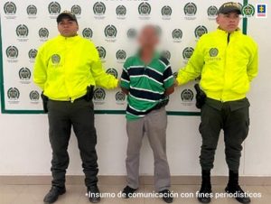 En la imagen aparece el capturado junto a dos uniformados de la Policía Nacional. En la parte posterior se aprecia el banner que identifica a la Policía Nacional.