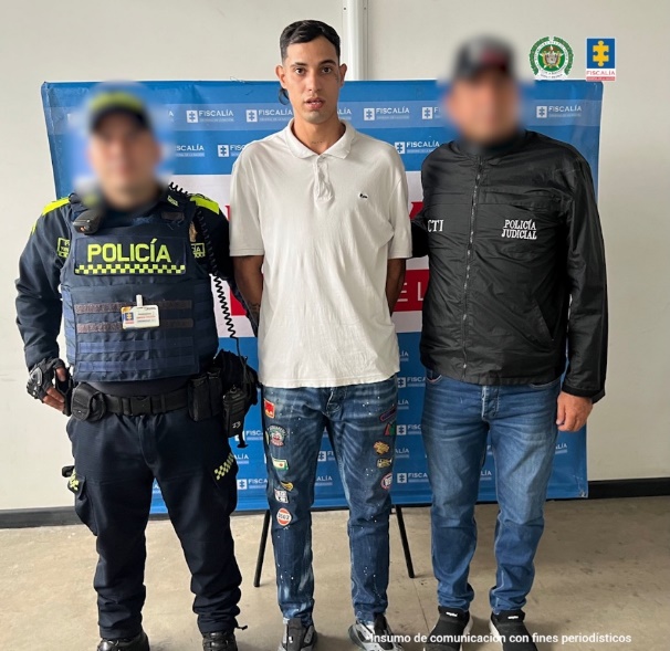 Se visualiza al capturado junto a un uniformado y un investigador del CTI. Detrás de ellos el banner que identifica a la Fiscalía General de la Nación.