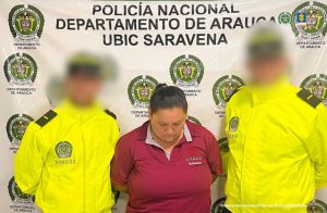 Se visualiza a la capturada junto a dos uniformados de la Policía Nacional. Detrás de ellos el banner institucional que identifica a la Policía Nacional en Saravena (Arauca)
