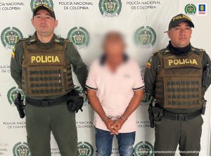 En la imagen aparece el capturado junto a dos uniformados de la Policía Nacional. En la parte posterior se aprecia el banner que identifica a la Policía Nacional.