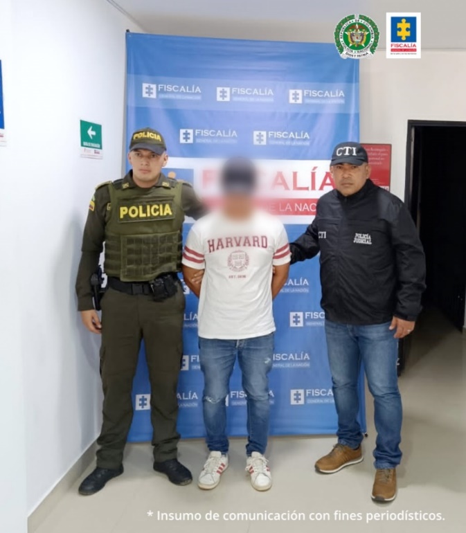 En la imagen se observa al capturado junto a un uniformado de la Policía Nacional y un investigador del Cuerpo Técnico de Investigación. En la parte posterior el banner que identifica a la Fiscalía General de la Nación