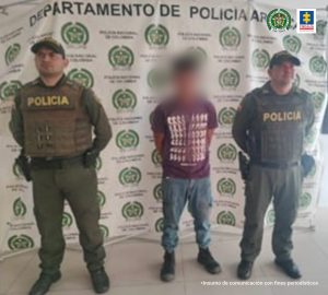En la imagen se observa al capturado junto a dos uniformados de la Policía Nacional. Detrás de ellos un banner que identifica al Departamento de Policía de Arauca.