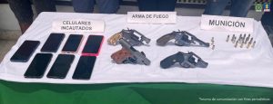 Se visualiza una mesa con los elementos incautados como: celulares, armas de fuegos y munición.