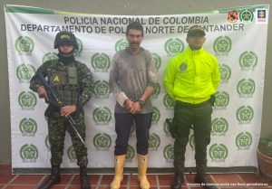 En la imagen se aprecia al capturado junto a dos uniformados de la Policía y Ejército Nacional: Detrás se visualiza el banner que identifica al Departamento de Policía de Norte de Santander