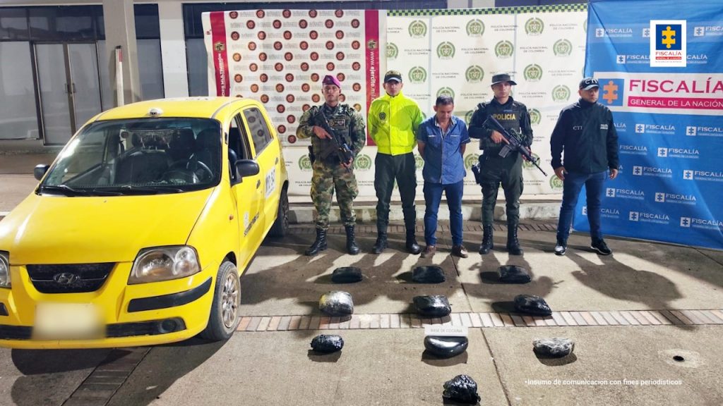En la imagen se ve una persona detenida bajo custodia de integrantes del CTI de la Fiscalía, Policía y Ejército. Frente a ellos varias bolsas con sustancia estupefaciente y un taxi. Detrás, un backing de cada una de las instituciones.