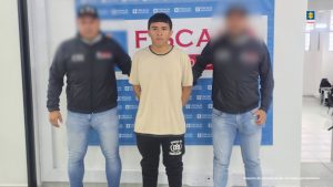 En la imagen se ve un hombre detenido bajo custodia de dos investigadores del CTI. Detrás suyo un backing institucional