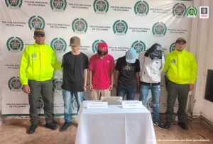 Se observan cuatro capturados en fila y a cada costado un funcionario de Policía NacionalAdelante una mesa con material incautado y atrás un pendón de Policía Nacional