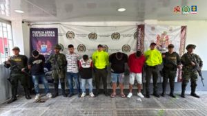 En la imagen se ven varias personas detenidas bajo custodia de uniformados de la Policía Nacional y el Ejército. Detrás suyo backings institucionales.