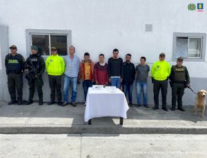 En la imagen se ven detenidas seis personas bajo custodia de integrantes de la Policía Nacional. Frente a ellos una mesa con elementos incautados.