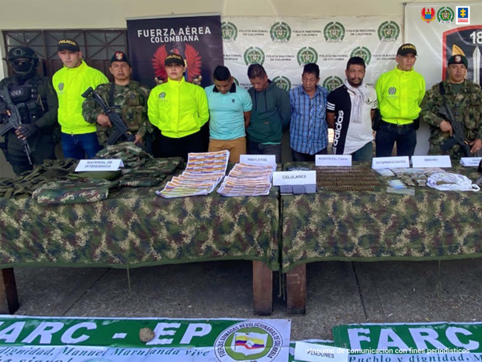 En la imagen se ven varias personas detenidas bajo custodia de la Policía Nacional, Ejército y Fuerza Aérea. Delante de ellos una mesa con varios elementos incautados y detrás, backings institucionales.