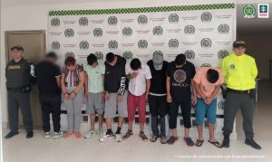 en la imagen se ven varias personas detenidas bajo custodia de integrantes de la Policía Nacional. Detrás suyo backings institucionales.