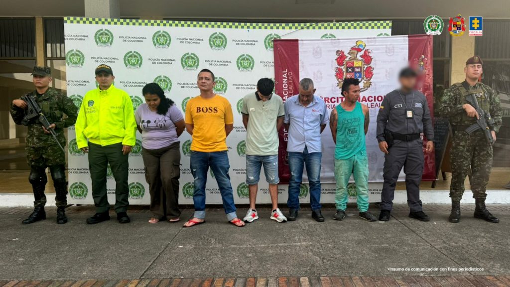en la imagen se ven cinco personas detenidas bajo custodia de integrantes del CTI, Policía y Ejército. Detrás suyo backings institucionales.