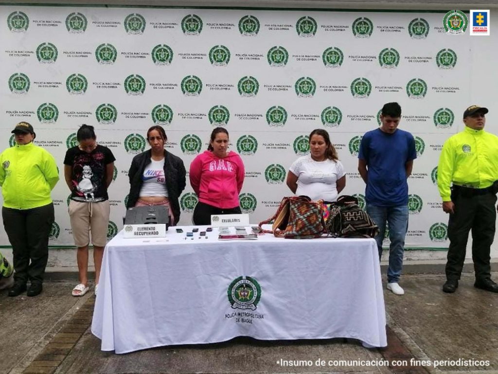 en la imagen se ve un grupo de personas detenidas bajo custodia de la Policía, detrás suyo un backing institucional.
