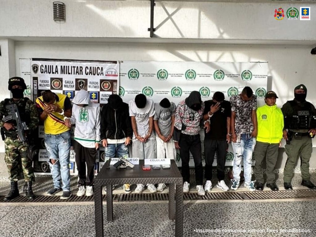 En la fotografía se observan ocho de los capturados junto a tres uniformados de la Policía Nacional. En la parte posterior se observa una mesa con una pistola y tres celulares