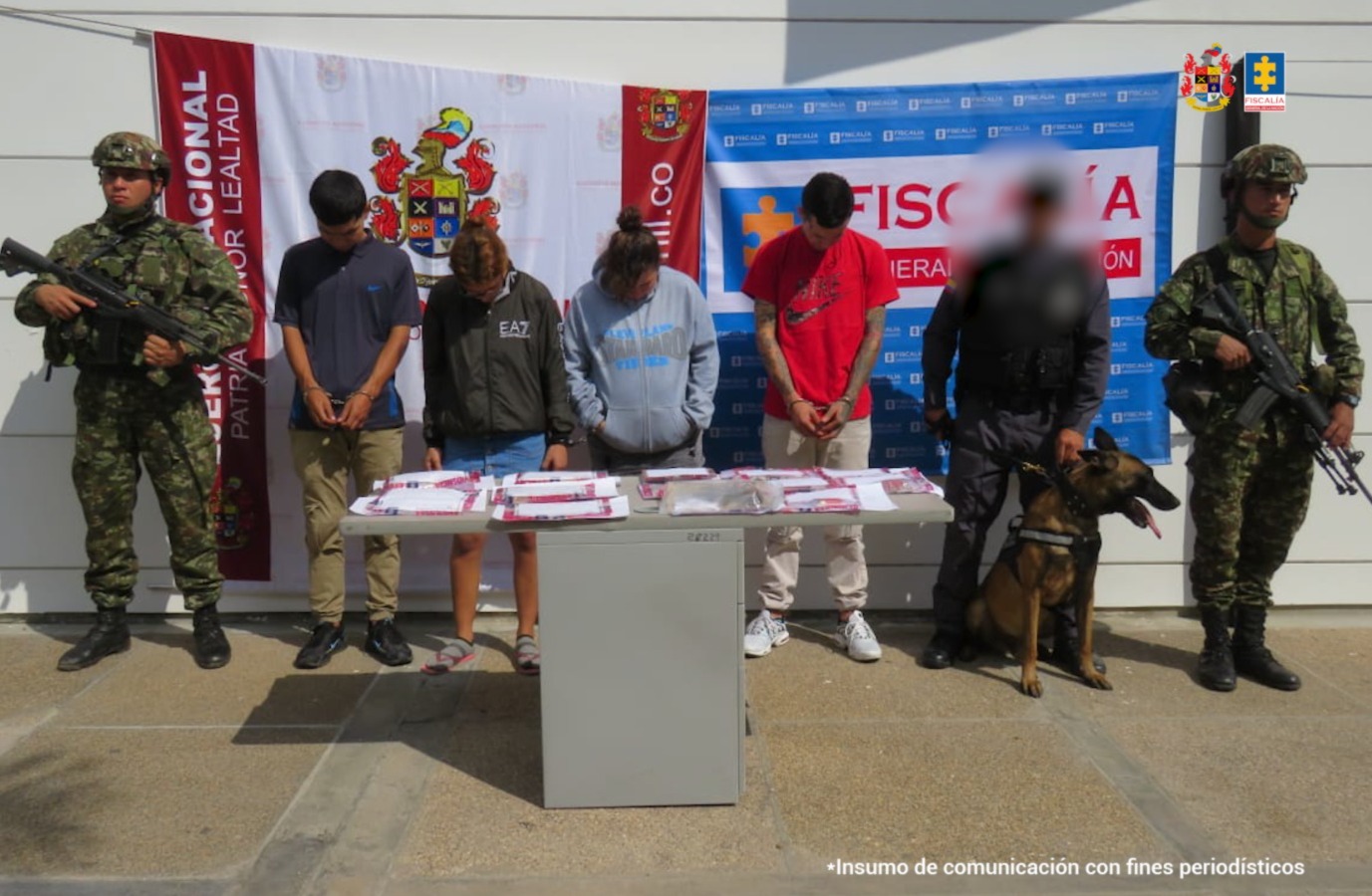 En la imagen hay varias personas detenidas bajo custodia de investigadores del CTI y el Ejército Nacional. Detrás suyo backings institucionales. Delante de ellos, una mesa con elementos incautados.