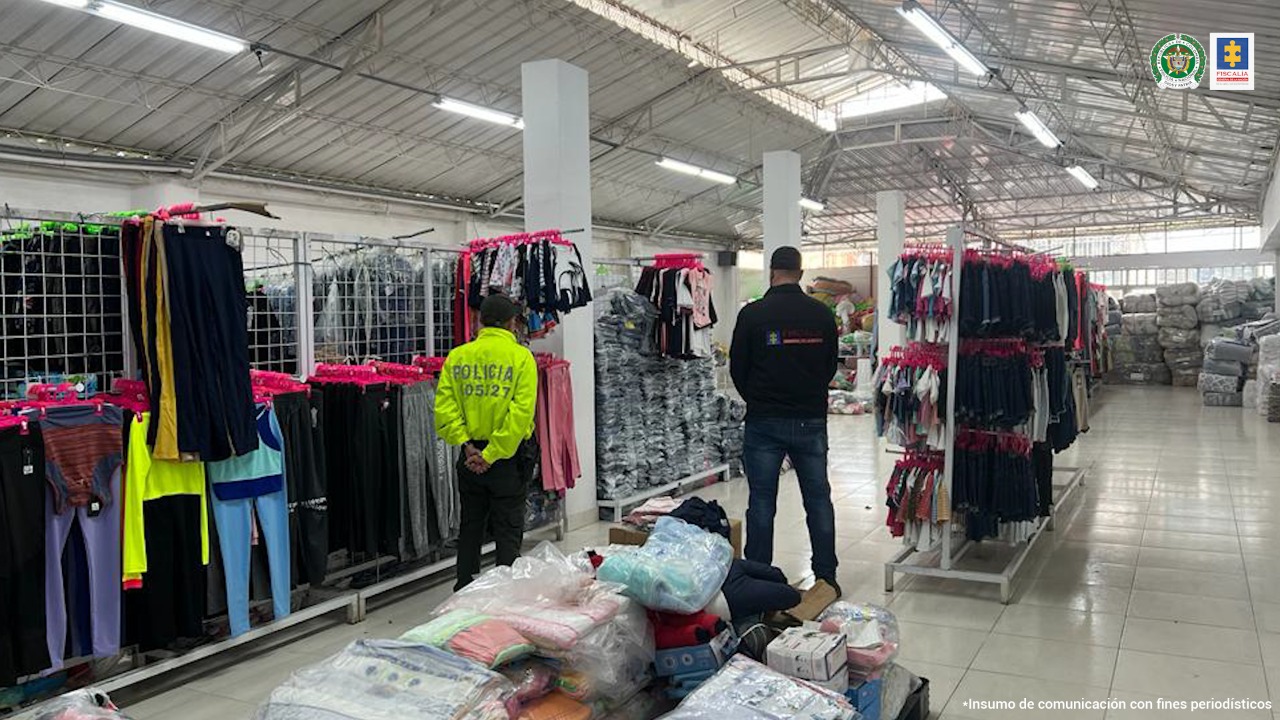Se ve una persona de la Policía y una persona del CTI. Al fondo se ve la mercancía textil incautada. 