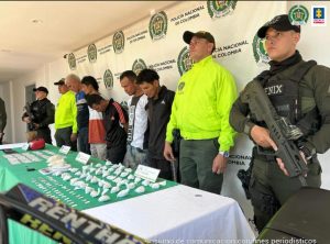 en la imagen se ven cinco personas detenidas bajo custodia de la Policía. Frente a ellos varios elementos incautados. Detrás suyo un backing de la Policía. 