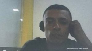 Hombre mirando la cámara y una pared blanca de fondo con una franja amarilla vertical.