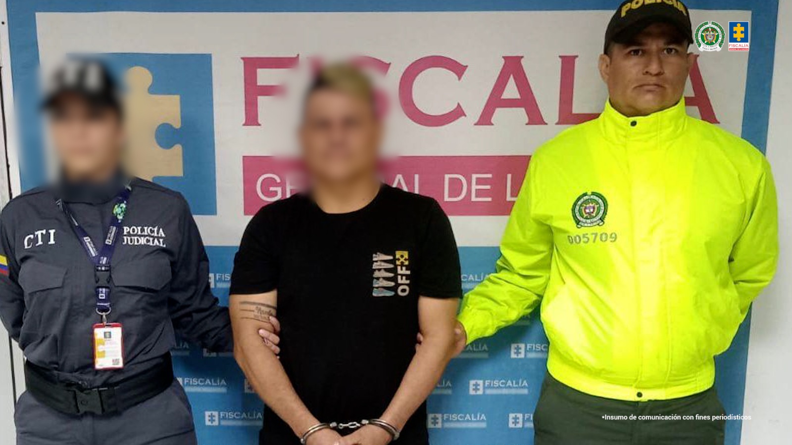 capturado de frente custodiado por investigador del CTI de la Fiscalía y un policía. Detrás banner de la Fiscalía.