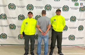 En la imagen aparece una persona capturada, de espaldas, entre dos uniformados de la Policía.