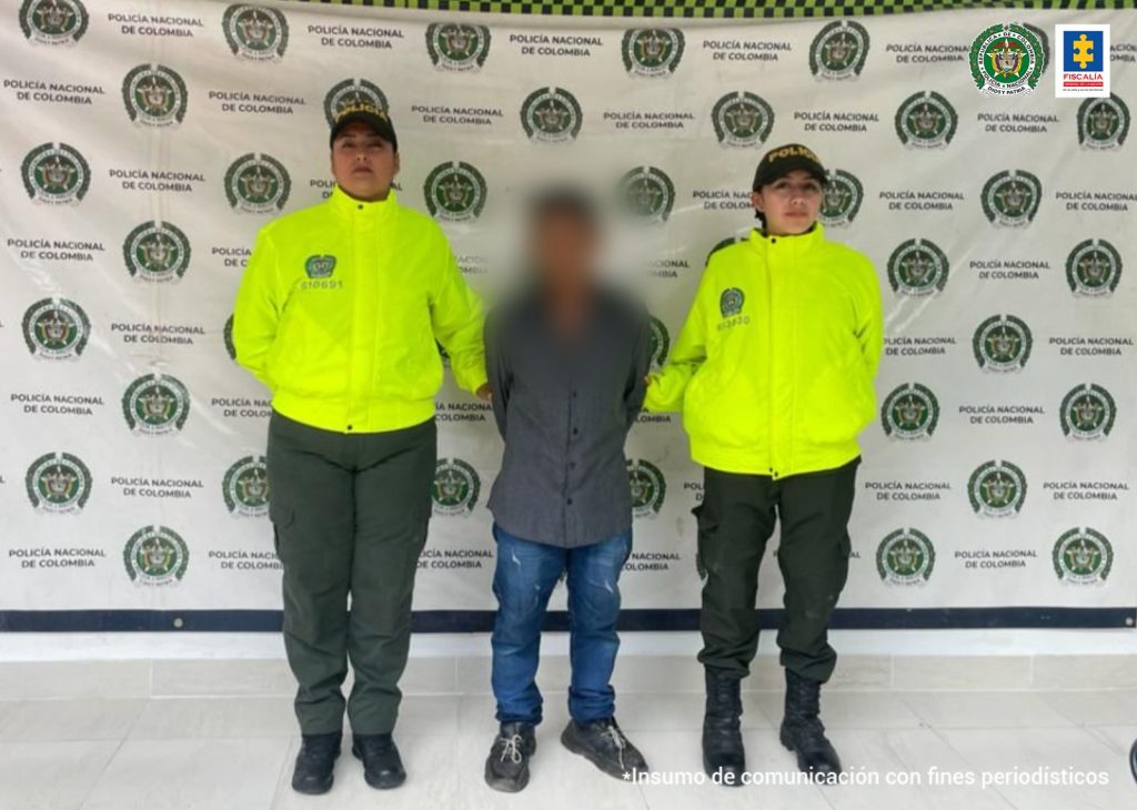En la imagen se ve una persona detenida bajo custodia de dos uniformados de la Sijin de la Policía Nacional. Detrás suyo un backing institucional.